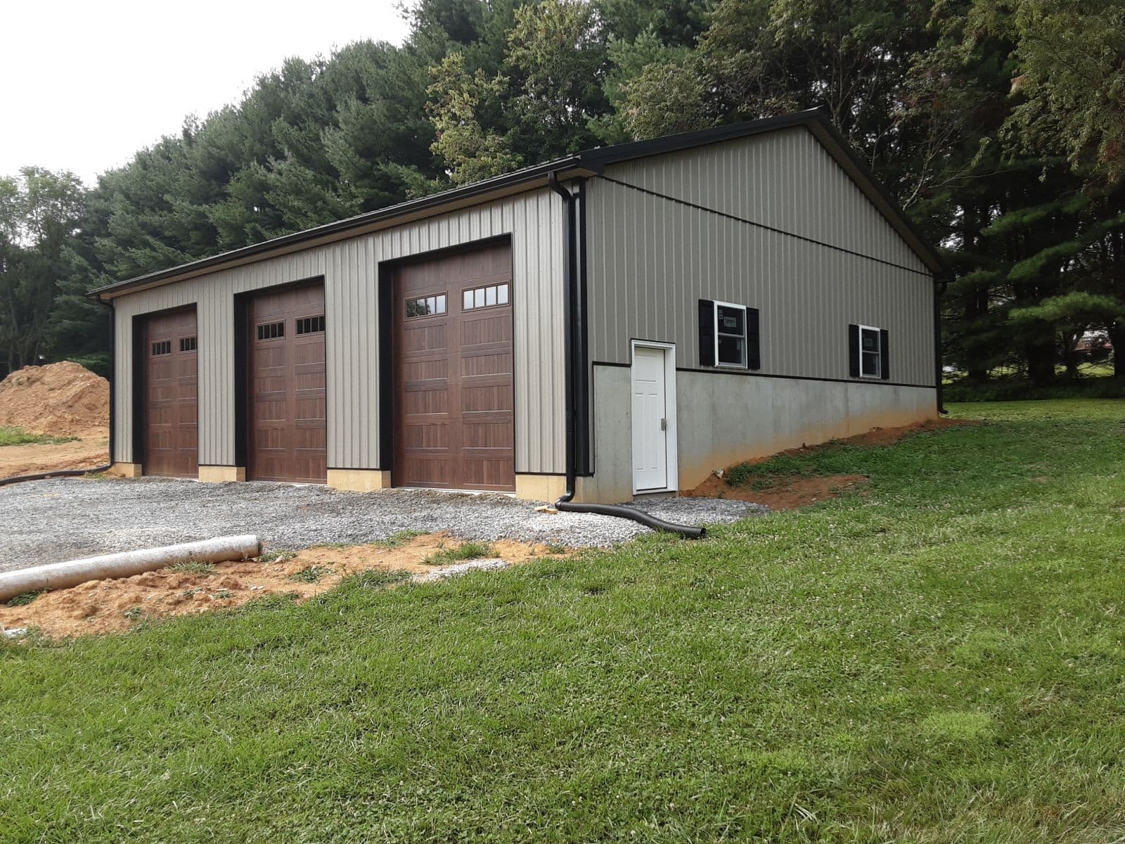A light gray pole building with black metal roof and trim and three large dark brown garage doors.