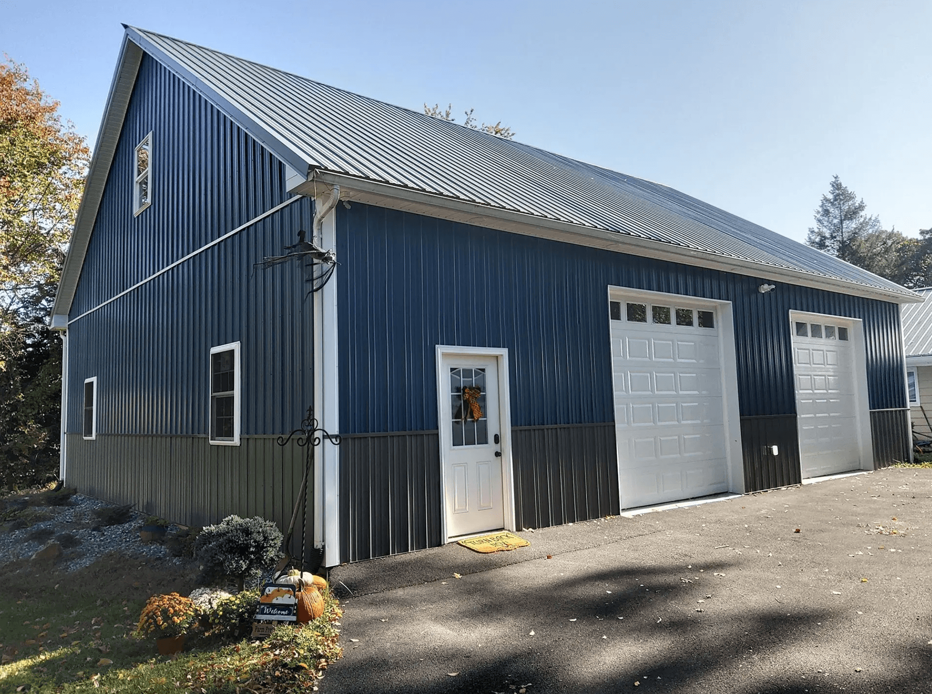 Dark blue metal pole barn with white trim, two garage doors, and a side entry door.