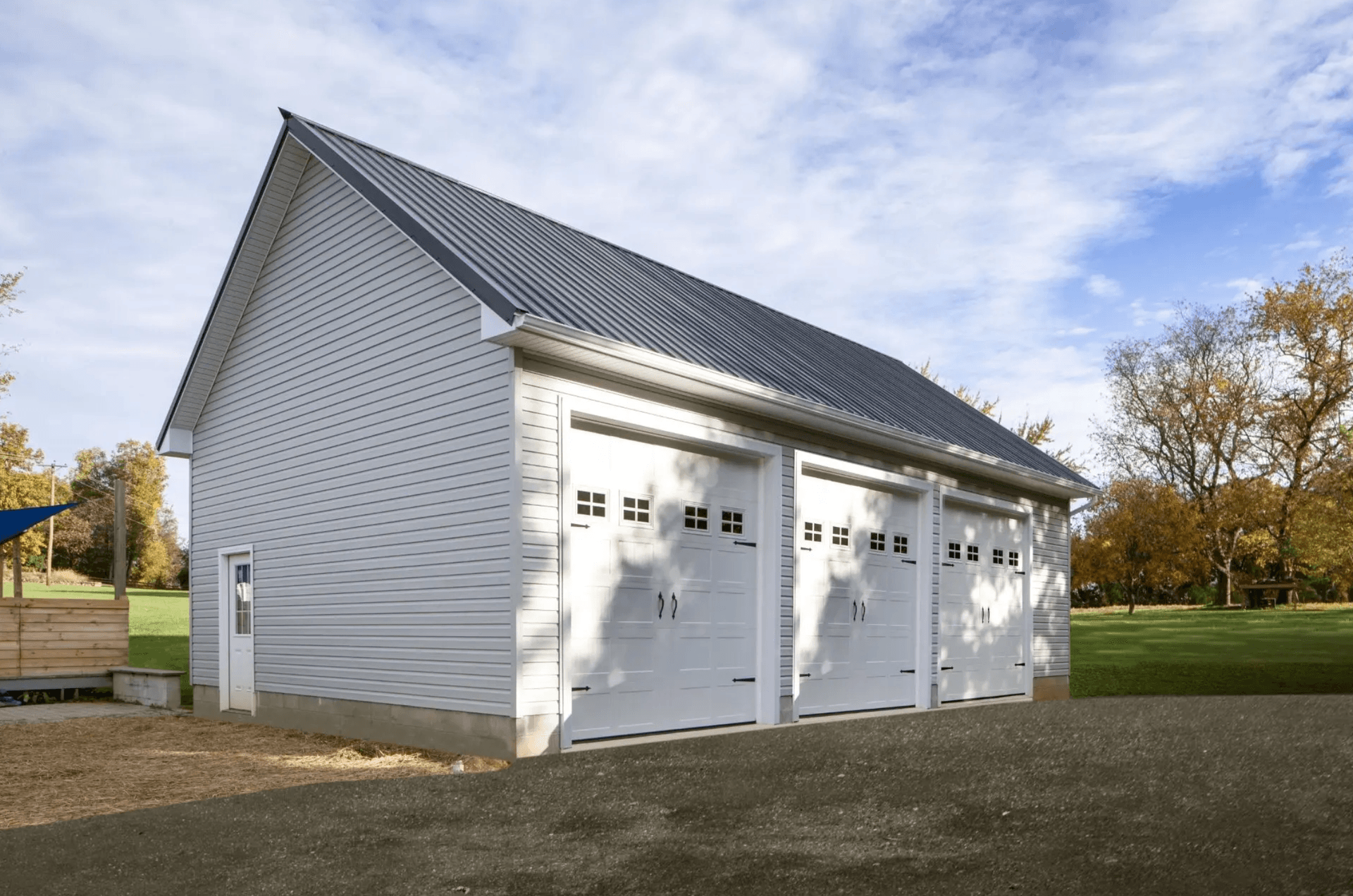 White pole barn with gray metal roofing, three garage doors, and a side entry door.