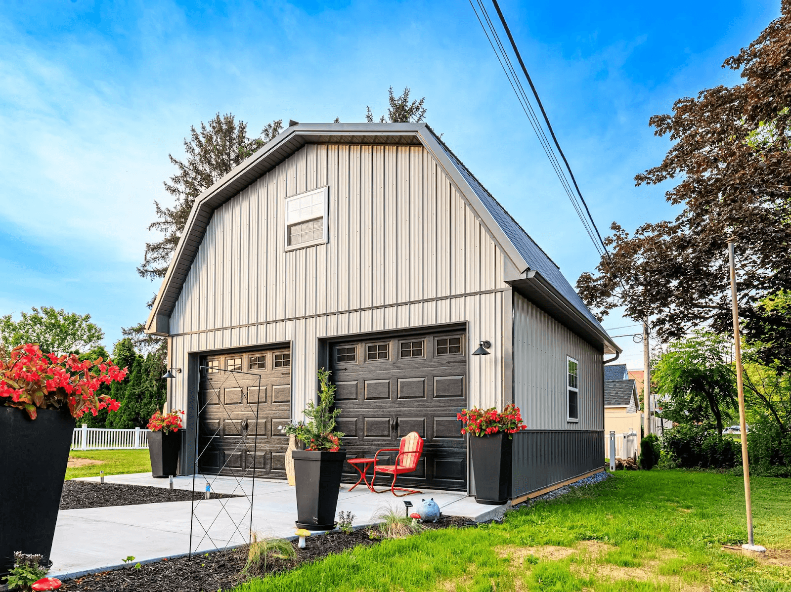 A finished garage with two black doors, large windows, and colorful flower pots in the front