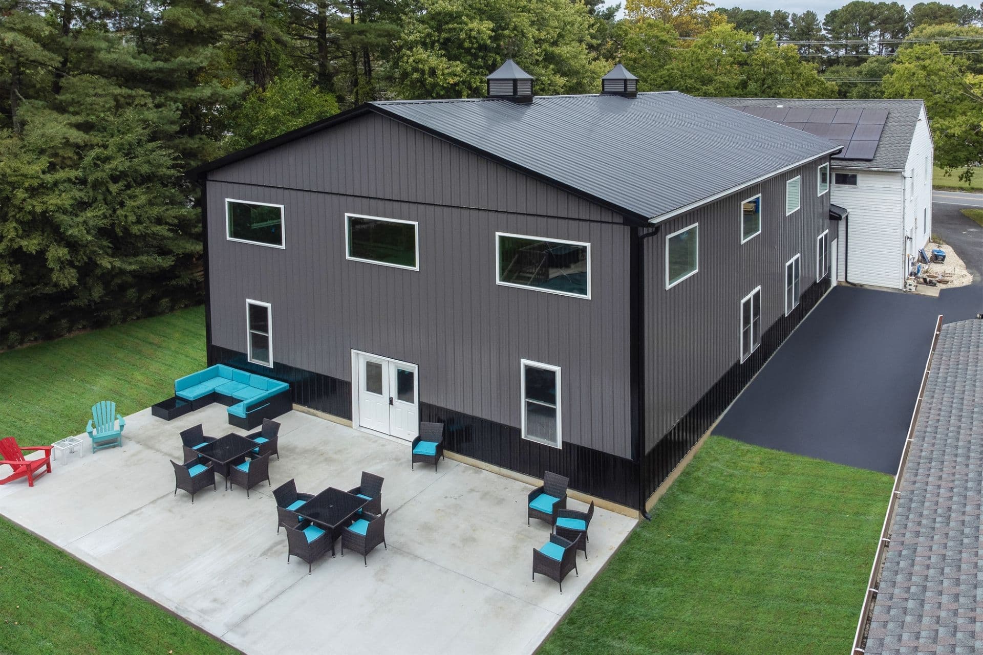 An aerial view of a gray and black barndominium with a patio and furniture out front.