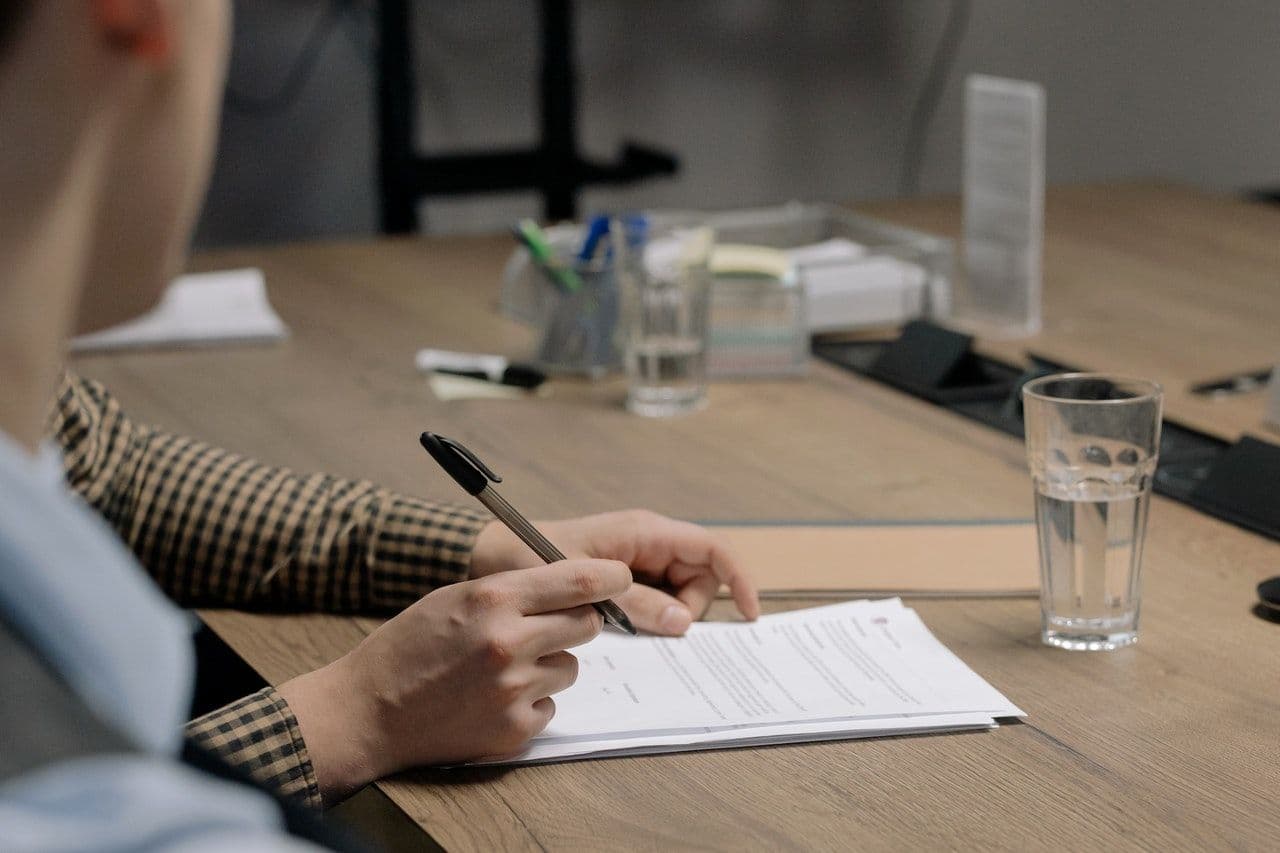 A person signs paperwork on a desk.