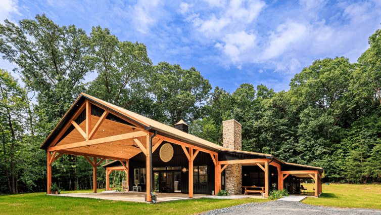 A black and brown barndominium with a large covered area and a chimney.