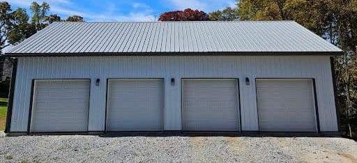A white post frame building with several garage doors.