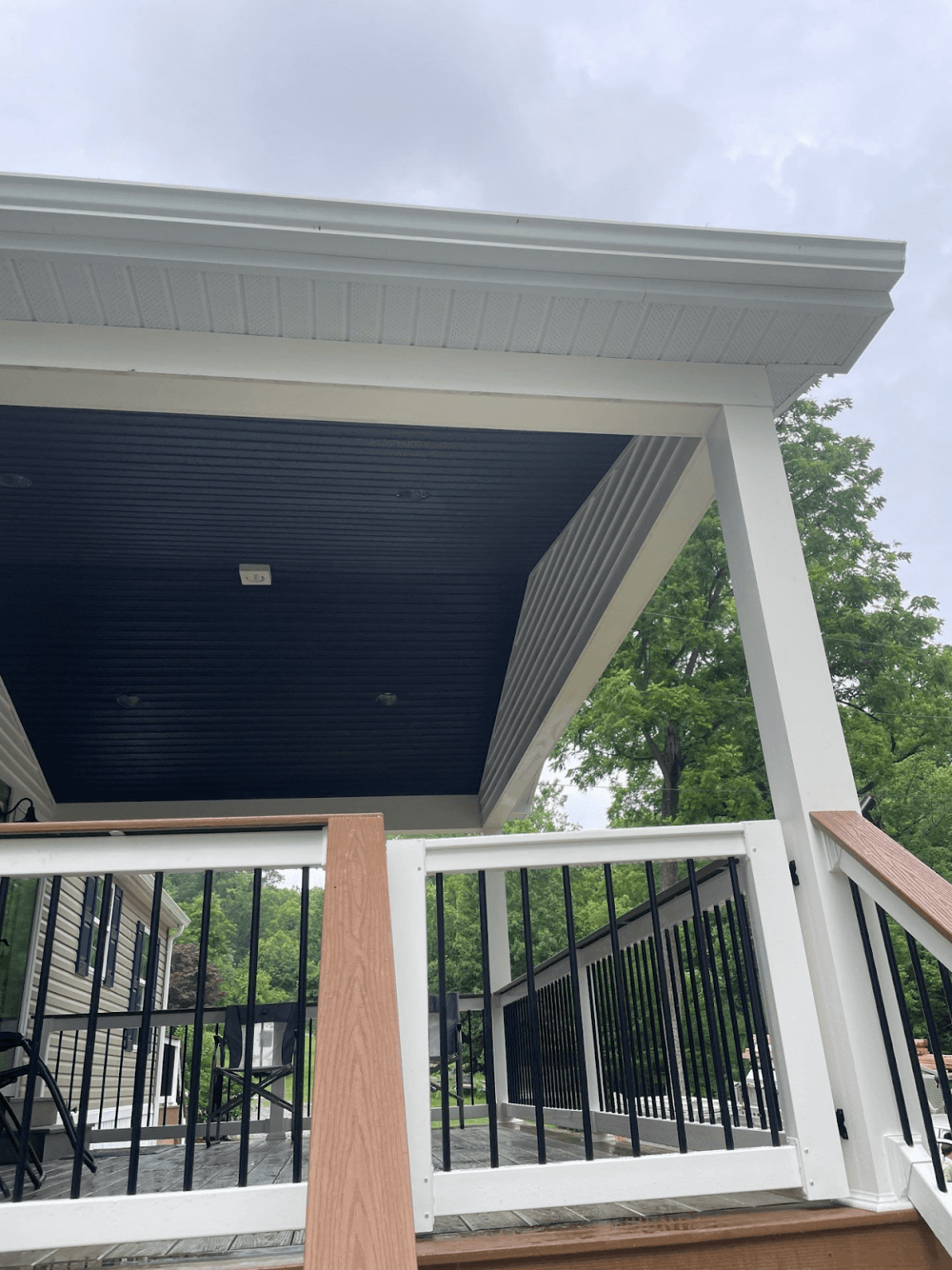 A new white covered porch and deck with black railings and interior roof.