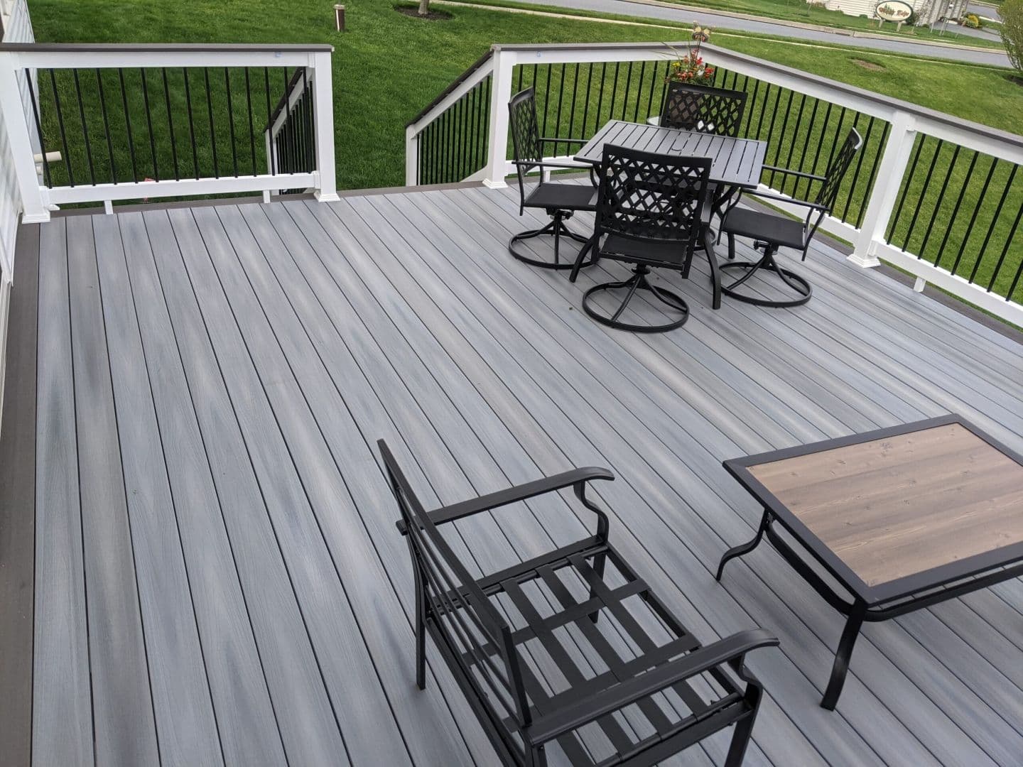 A light gray deck with white and black railings and black patio furniture.