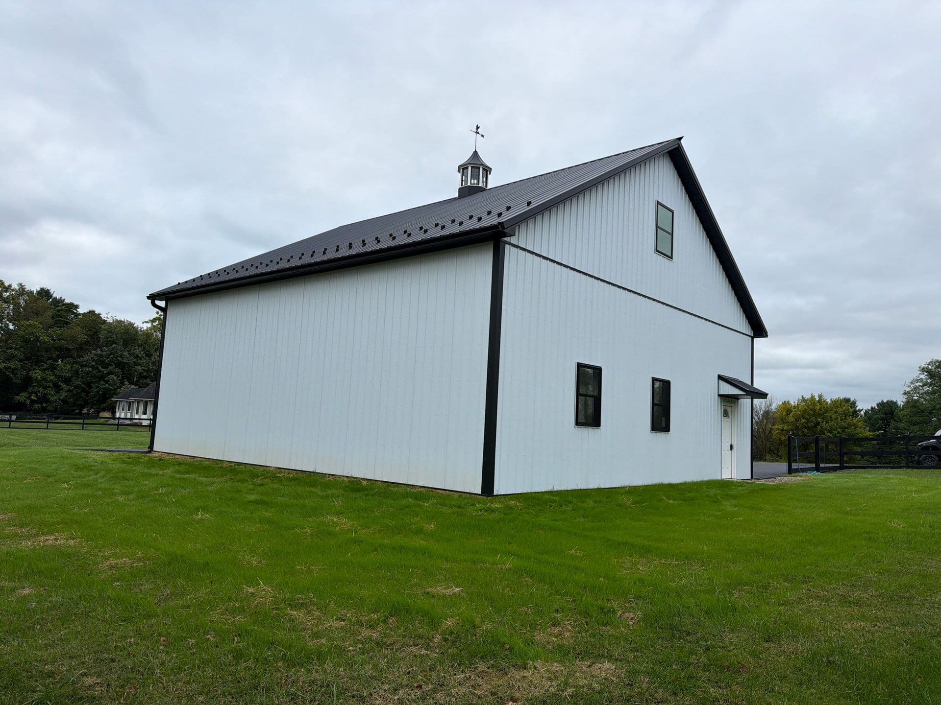 White barndominium with black metal roof and trim on a grassy property under an overcast sky.