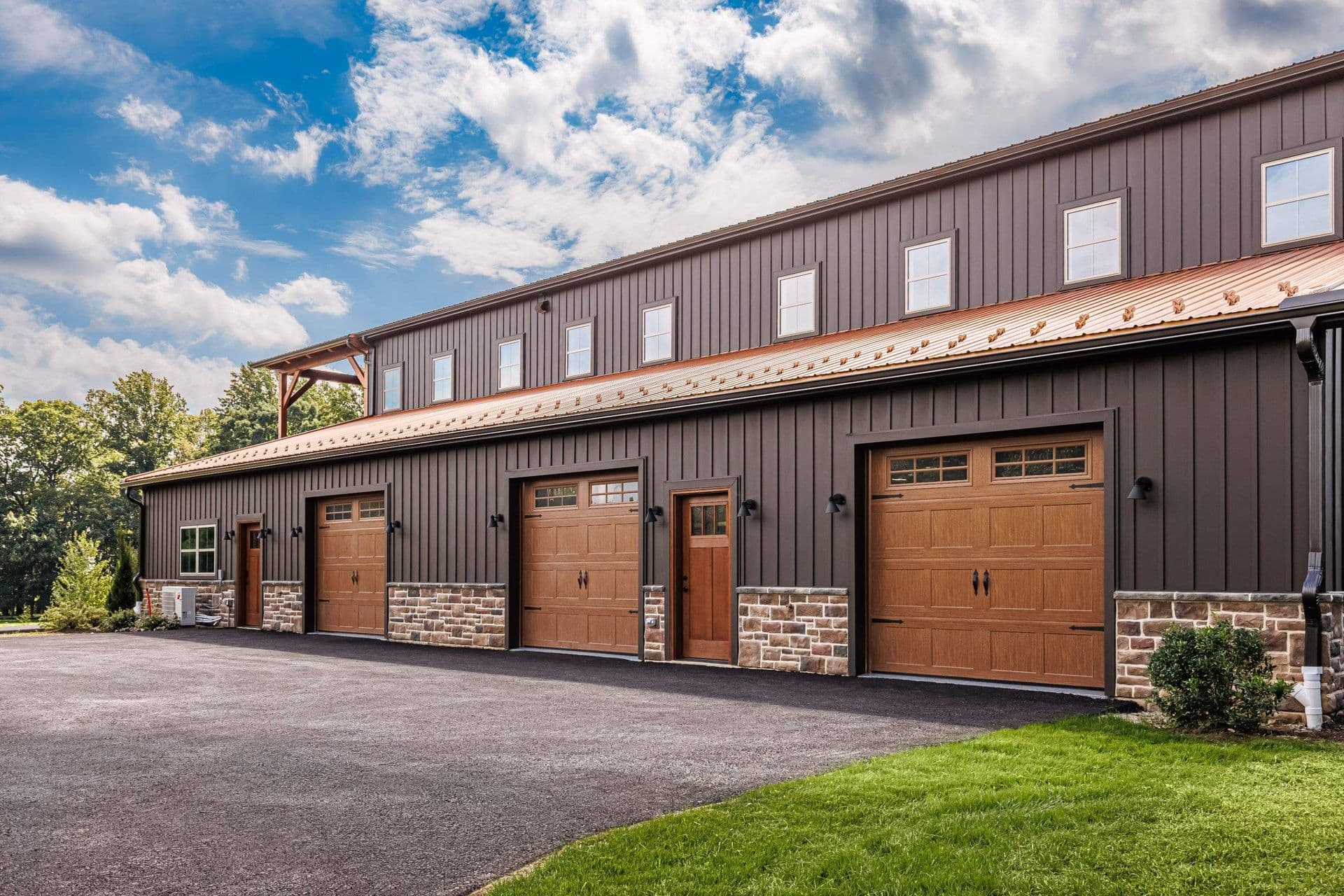 Large dark gray post-frame building with multiple wooden garage doors, windows, and a covered upper-level section.
