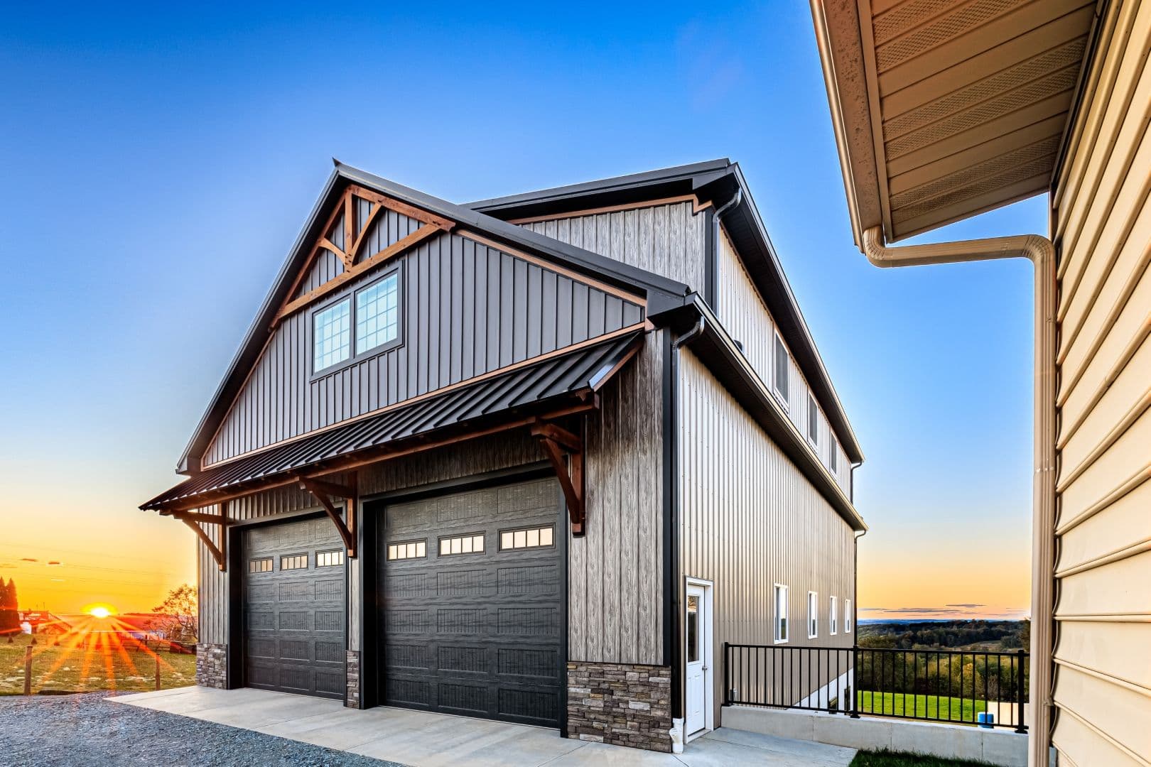 A dark gray barndominium with two black garage bay doors.