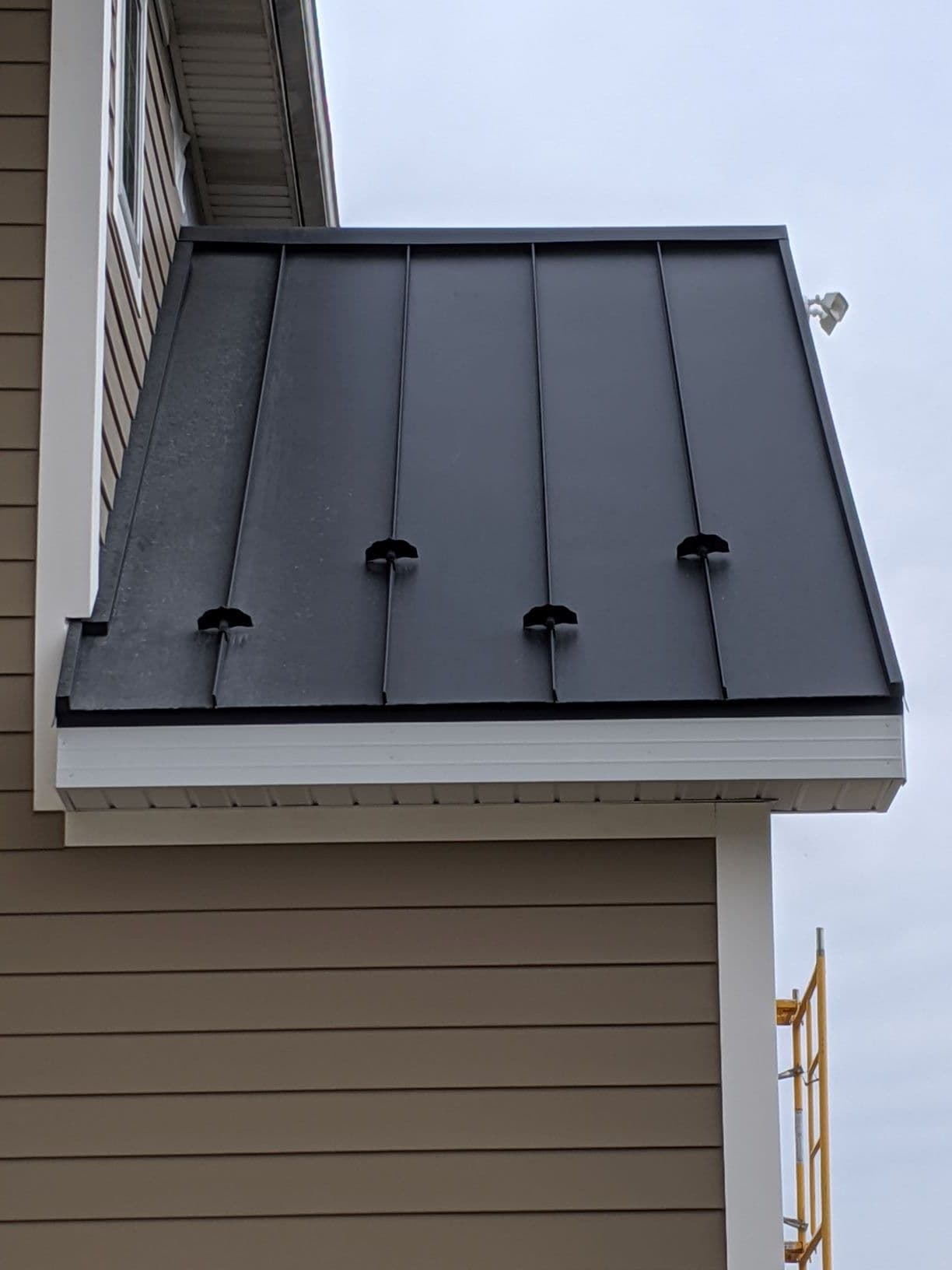 Details of a black metal roof on a tan building with white trim.
