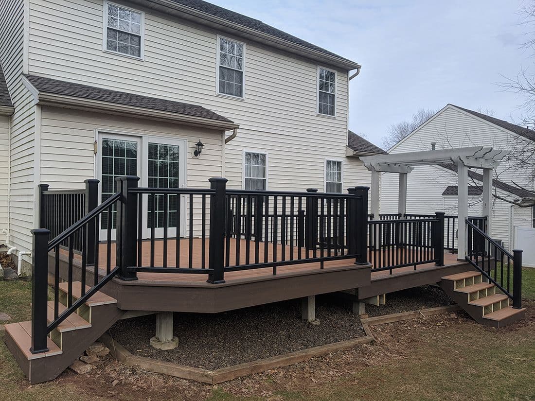 A brown deck with black metal railings and trim attached to a white house.