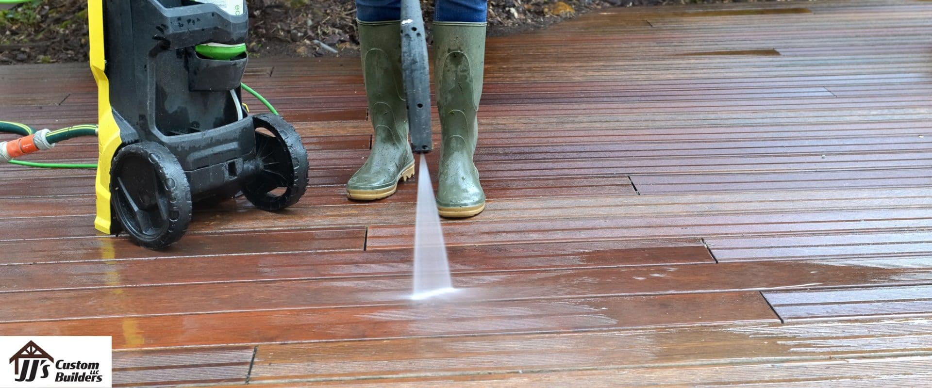 A person wearing green rain boots power washes a deck.