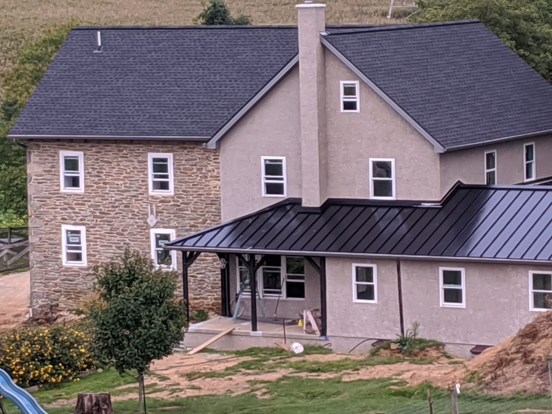 A stone and stucco house with a dark asphalt shingle roof and a porch with black metal roofing.