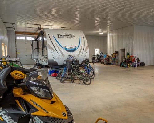 Large garage with a parked RV, several bicycles, a snowmobile, and various tools and equipment neatly arranged.