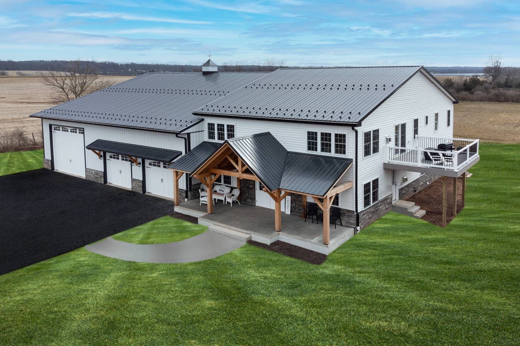 Large modern barn-style house with white siding, black metal roofing, three garage doors, a covered patio, and an elevated deck, situated on a green lawn in a rural setting.