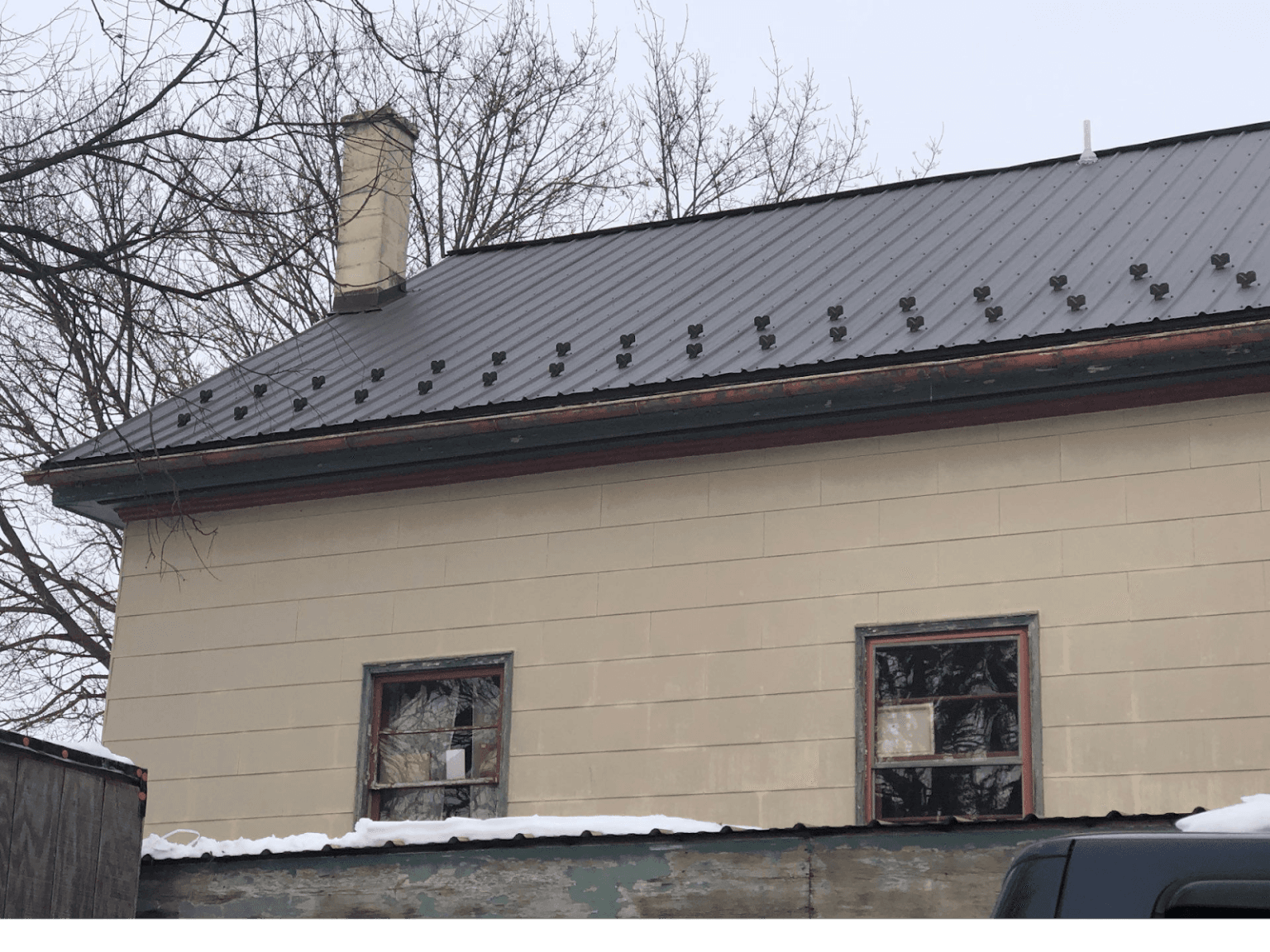 A beige house with newly-installed dark gray metal roofing.