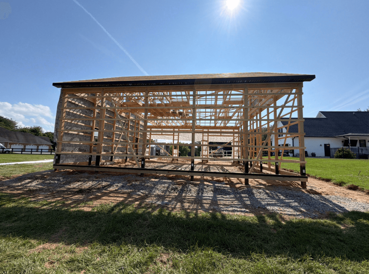 Partially constructed wooden-frame building with exposed roof trusses and framing under a bright blue sky.