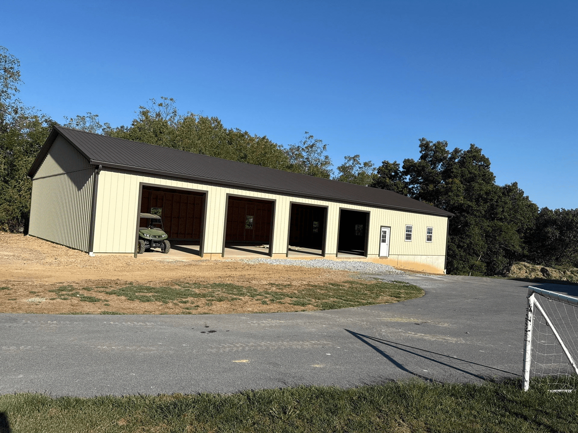 A light-colored four-bay pole barn garage with a black roof.