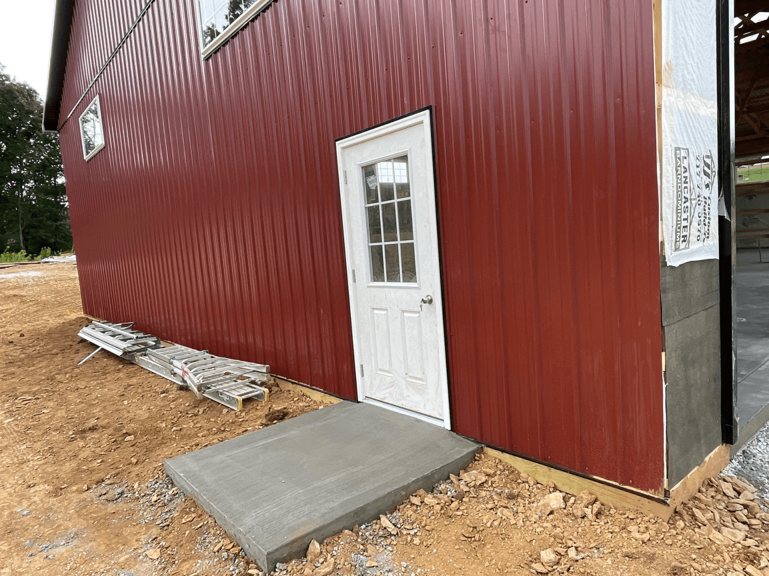 A red pole barn building with a white door under construction.