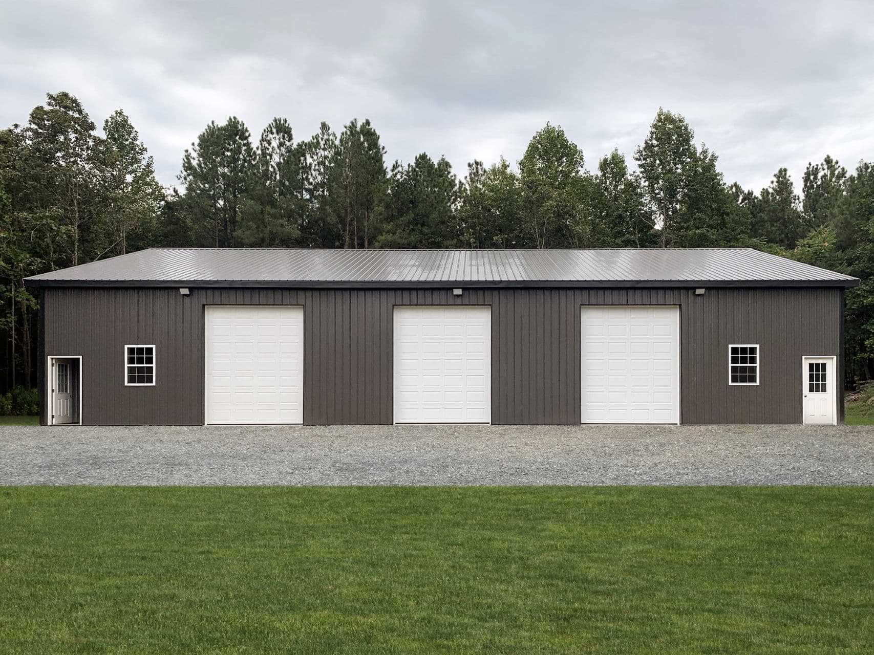 A long, dark gray barn warehouse space with three large white bay doors.