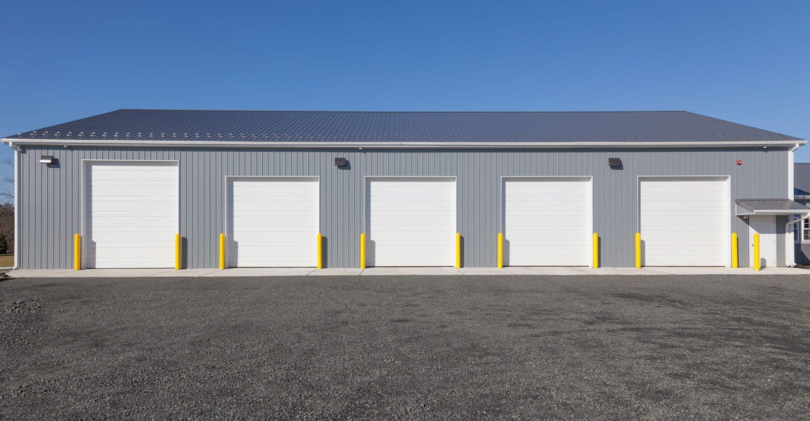 A gray commercial post frame building with multiple garage bays.