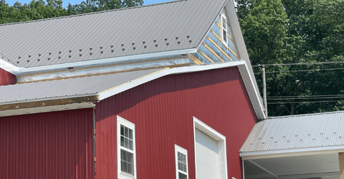 Roofing being installed on a red and white post frame building.