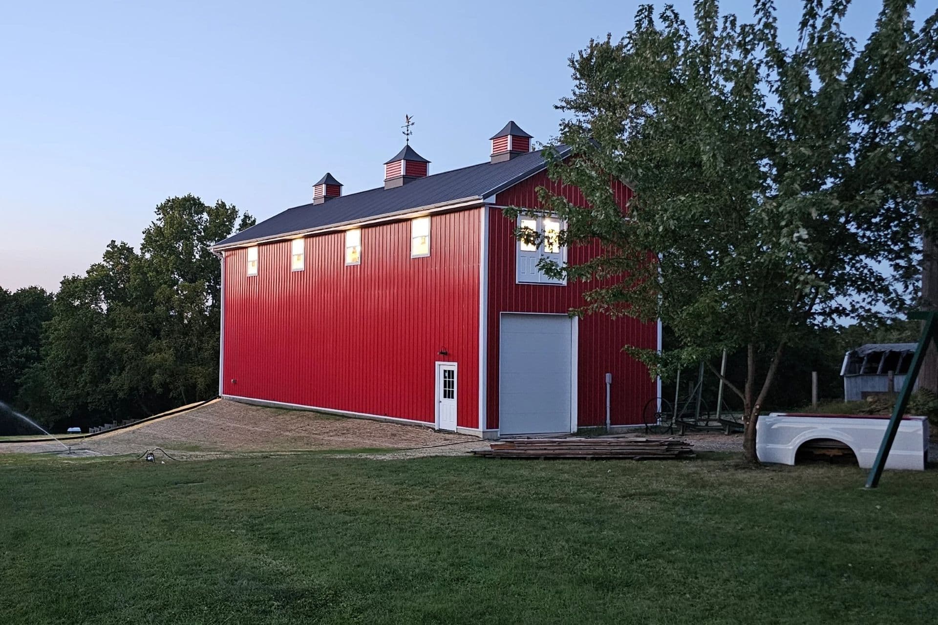 A two-story red post frame building with white garage door.