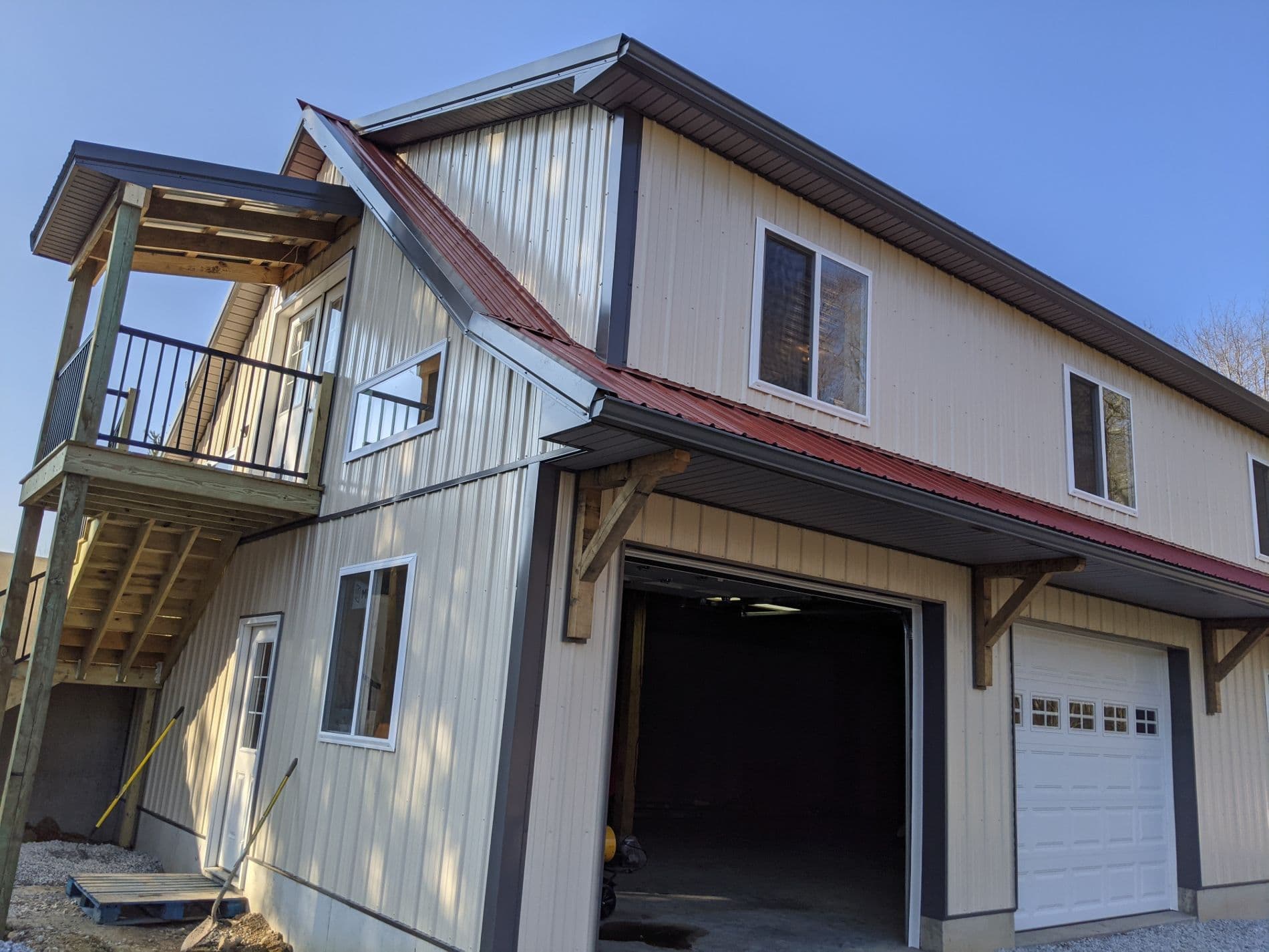 A light-colored pole building with a red metal roof and two garage bays.