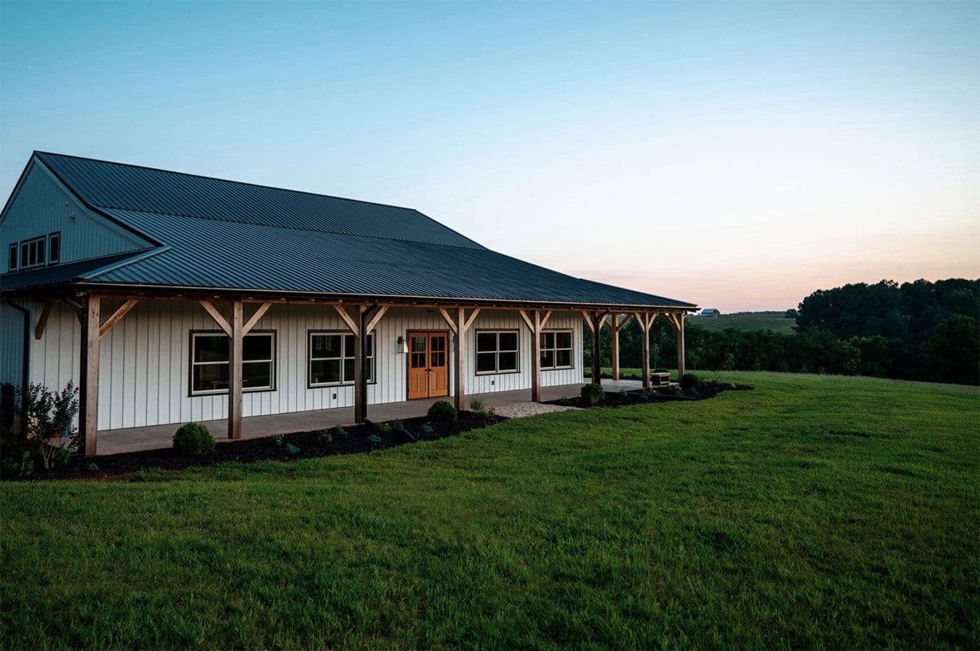 A white post frame building with black roof, multiple windows, and brown double doors.