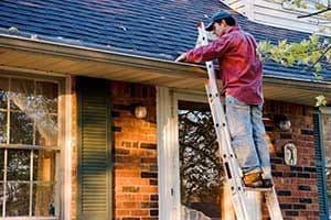 A person on a ladder cleaning gutters.