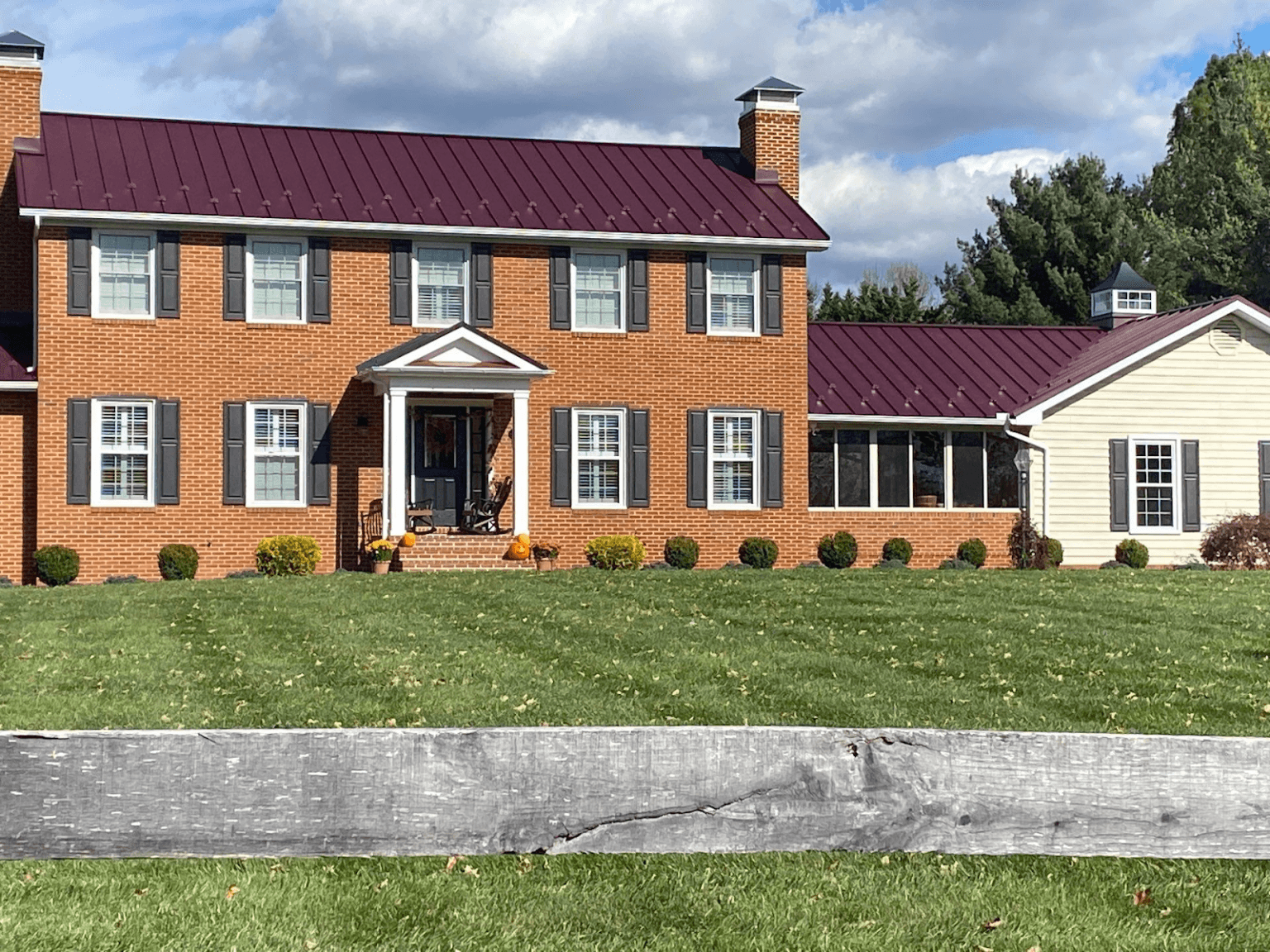A red brick house with dark red standing seam metal roof and a cupola.