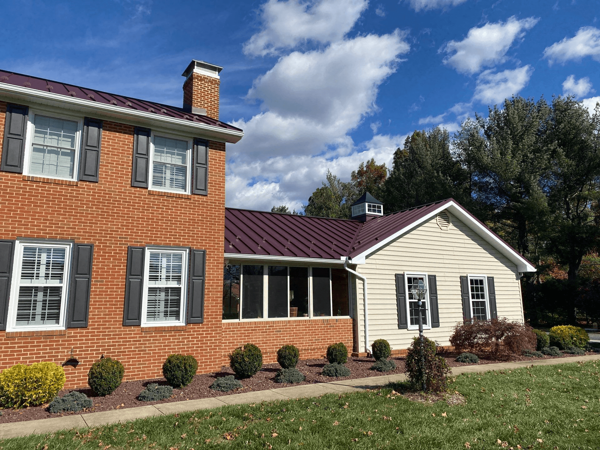 A red brick house with dark red standing seam metal roof and a cupola.