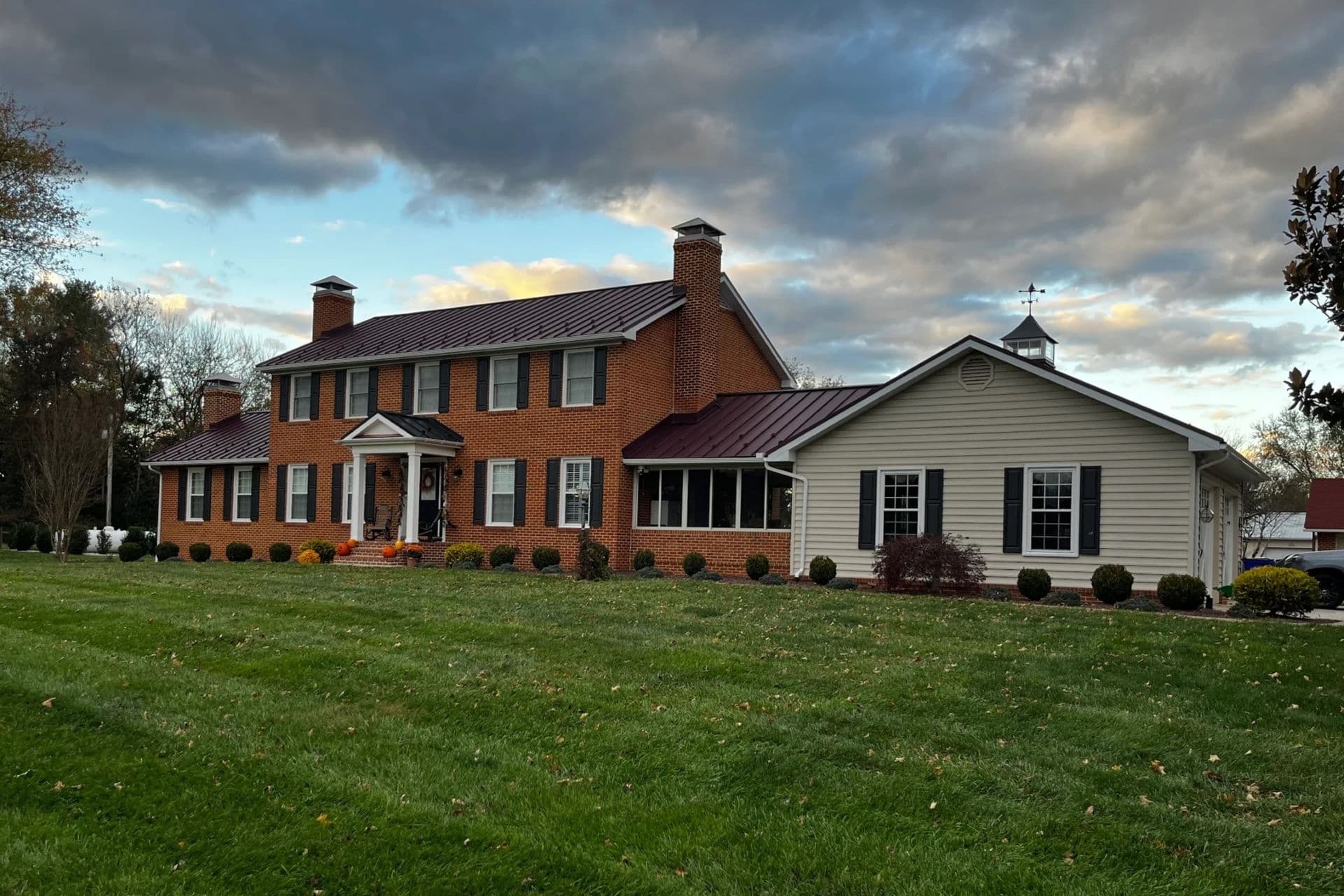 A red brick house with black standing seam metal roof and a cupola.