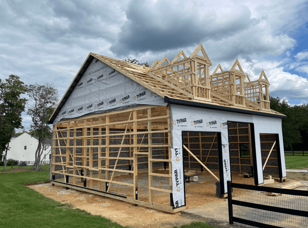 Wooden frame of a partially constructed two-story building with roof trusses and exterior house wrap