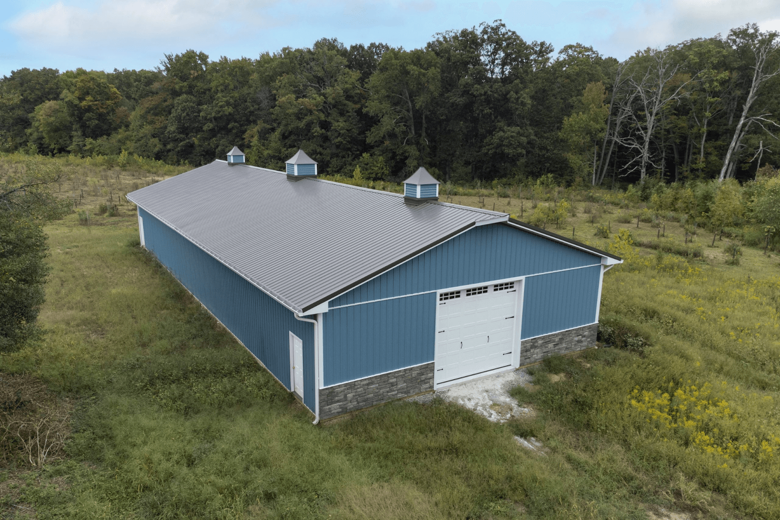 Blue metal outbuilding with gray roof in a grassy field.